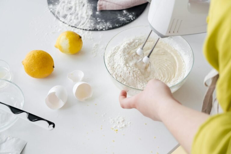 From above of crop anonymous female with mixer preparing cake dough at table with fresh lemons and eggshells in house